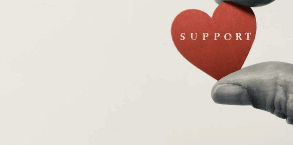 赤いハート型のカードに「SUPPORT」と書かれたものを指で持つ手
